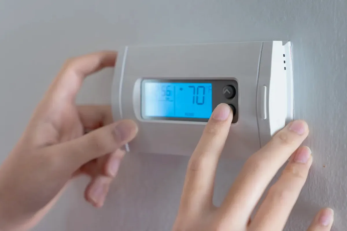 Hands adjusting a digital wall thermostat